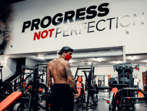 Brian Mark looks back over his shoulder. Part of the Iron Energy wall mural is highlighted in front of him, reading "PROGRESS NOT PERFECTION".